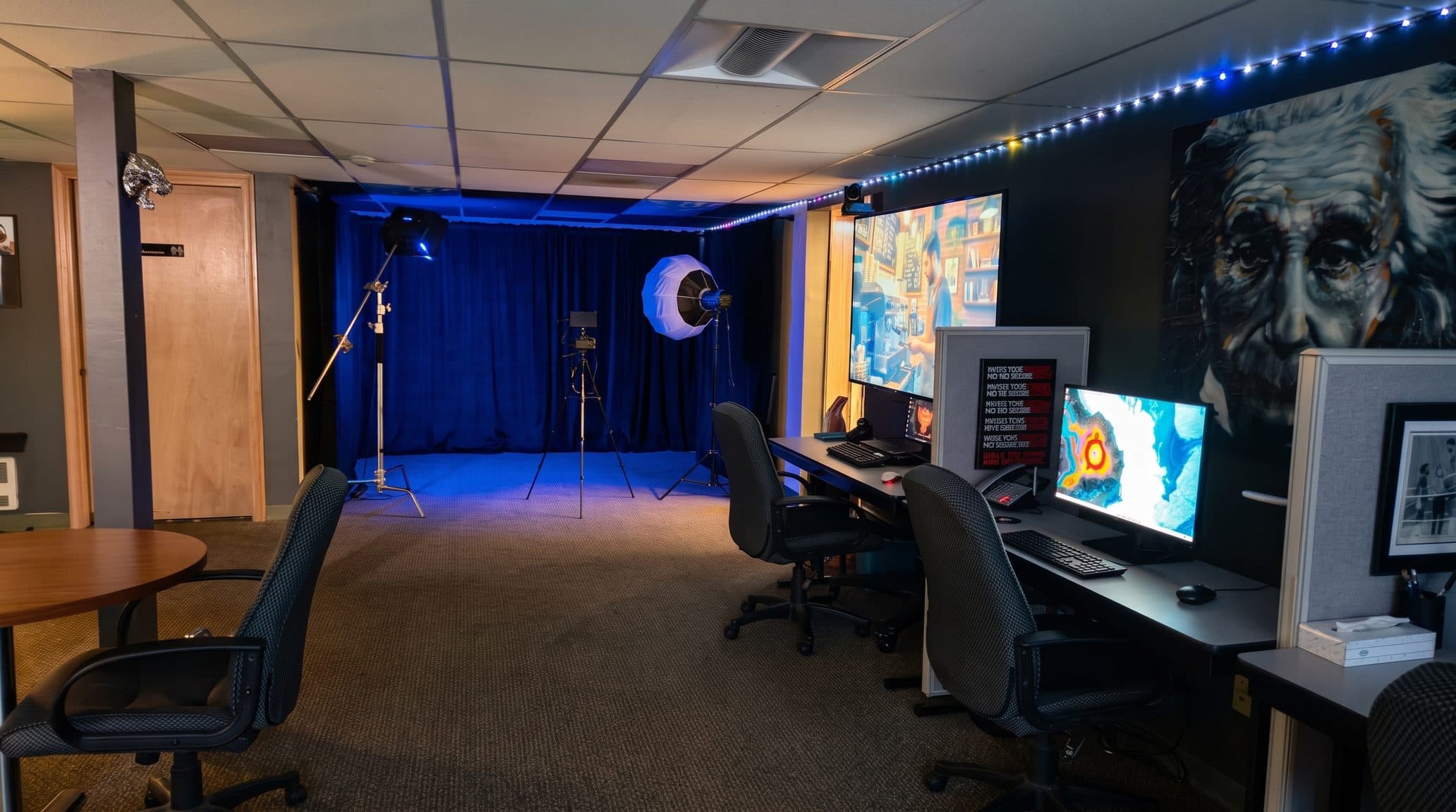 The main room, with a lit backdrop and lighting stands at one end and a row of editing desks along the wall at the other
